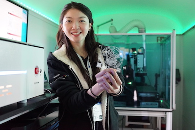 In the mobile lab interior, a student is showing a laser-engraved and cut plastic piece.
